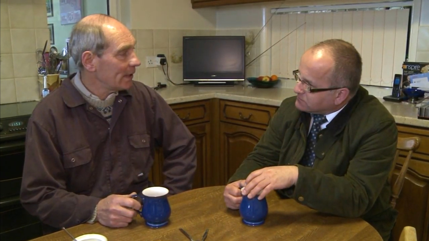 Rev Alan Robson sat at a kitchen table with a farmer