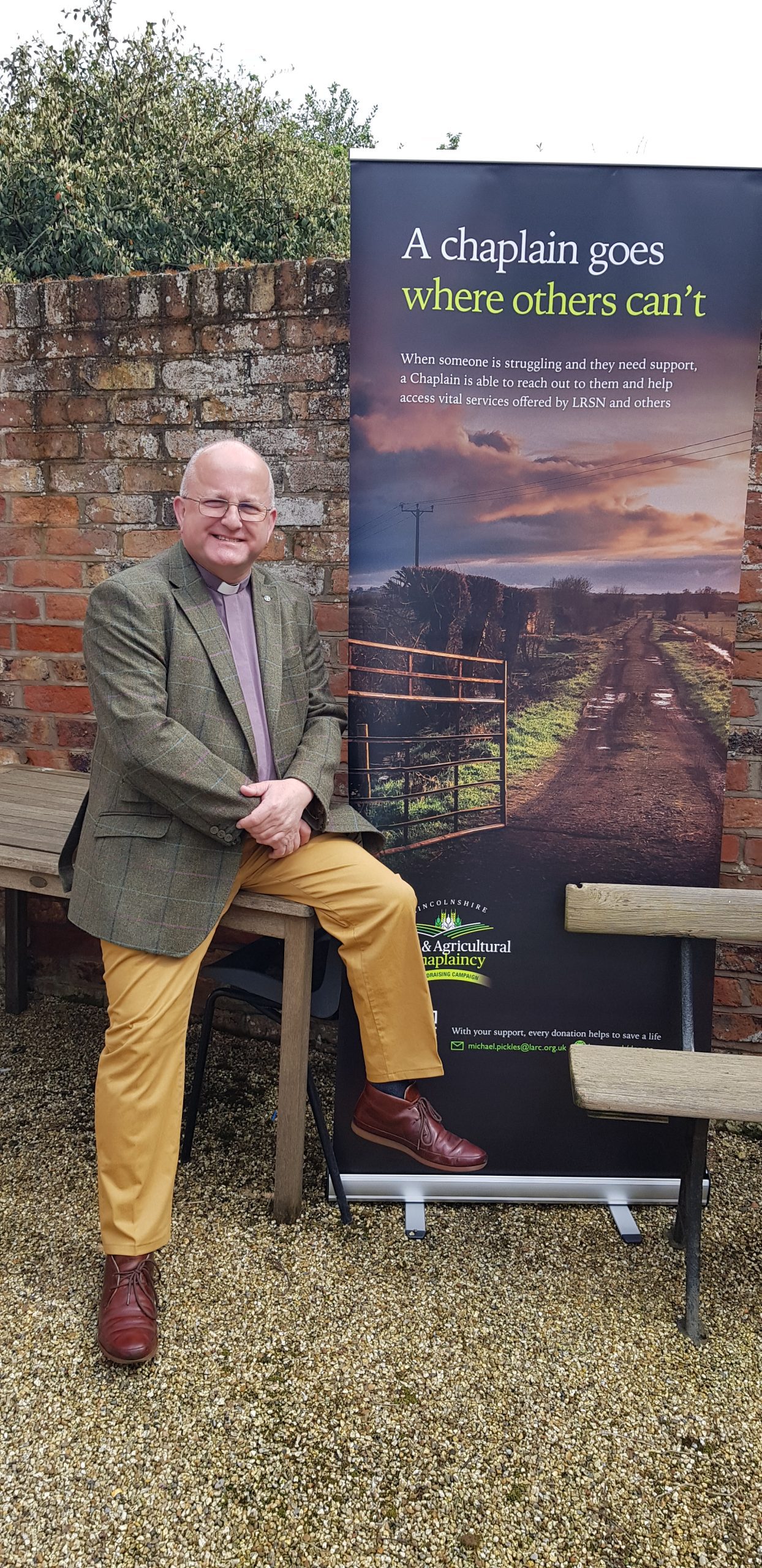 Rev'd Canon Alan Robson perched on the edge of a table next to the LRAC banner